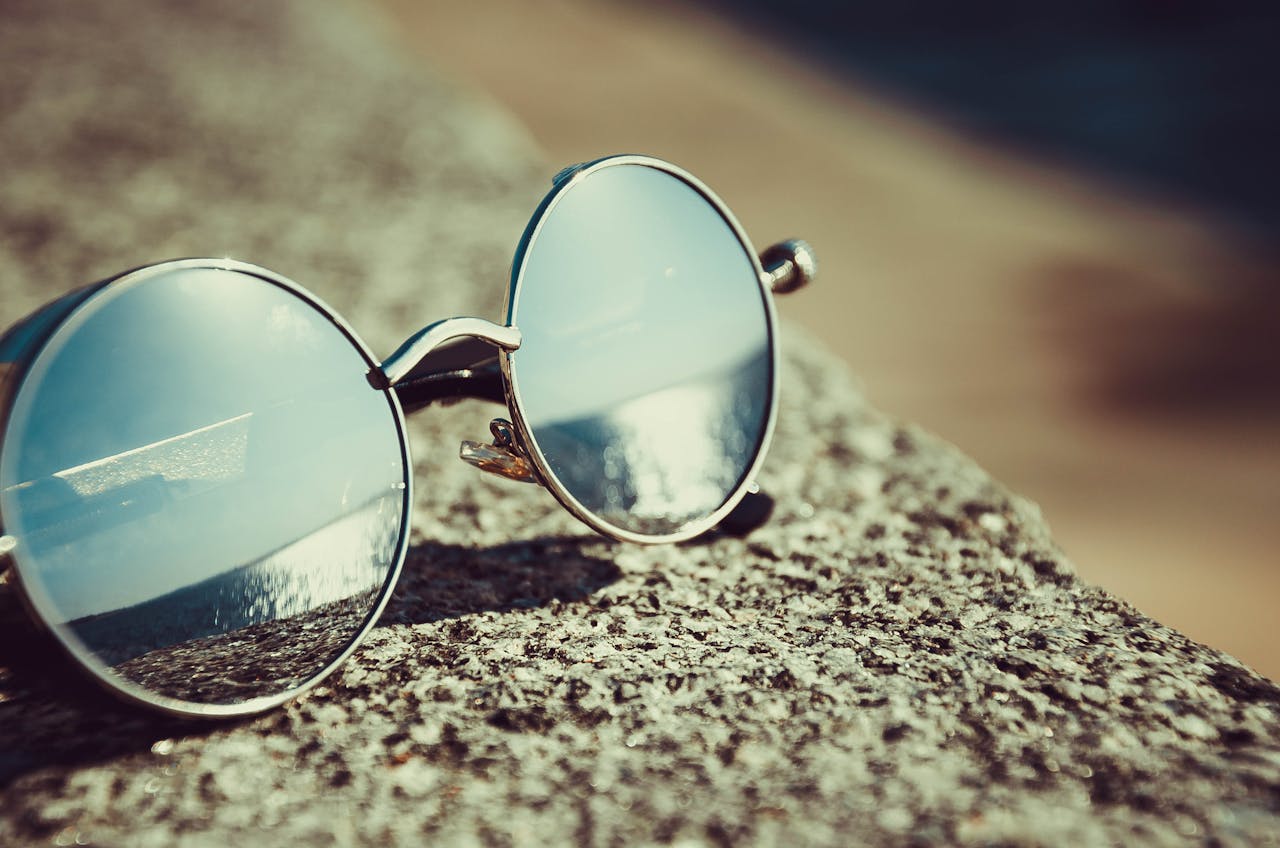 Home Round sunglasses resting on a sandy beach reflecting the ocean view.